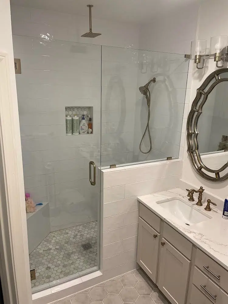 Frameless glass shower door and panel with brushed brass handle in a white subway-tile bathroom